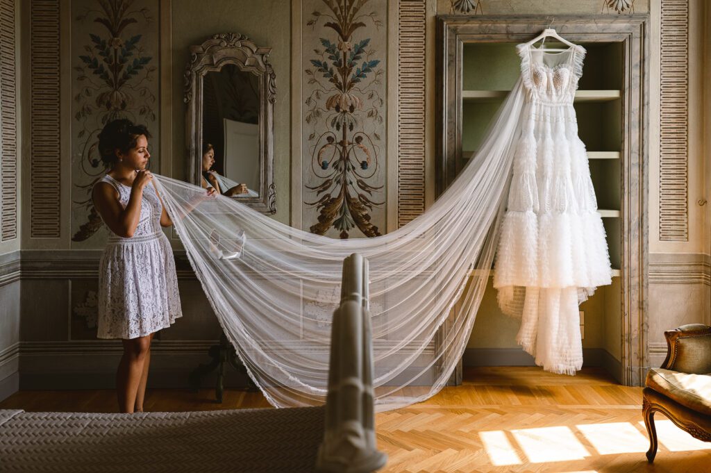 In a room reserved for the Wedding at Palazzo Gambara, the bride takes the veil in her hands and takes a look at her wedding dress before wearing it.